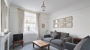 A living room with a fireplace, a television, a wooden coffee table, a grey sofa, and framed pictures on the wall.