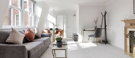 A modern living room with a grey sofa, a small table with a plant, and a fireplace.