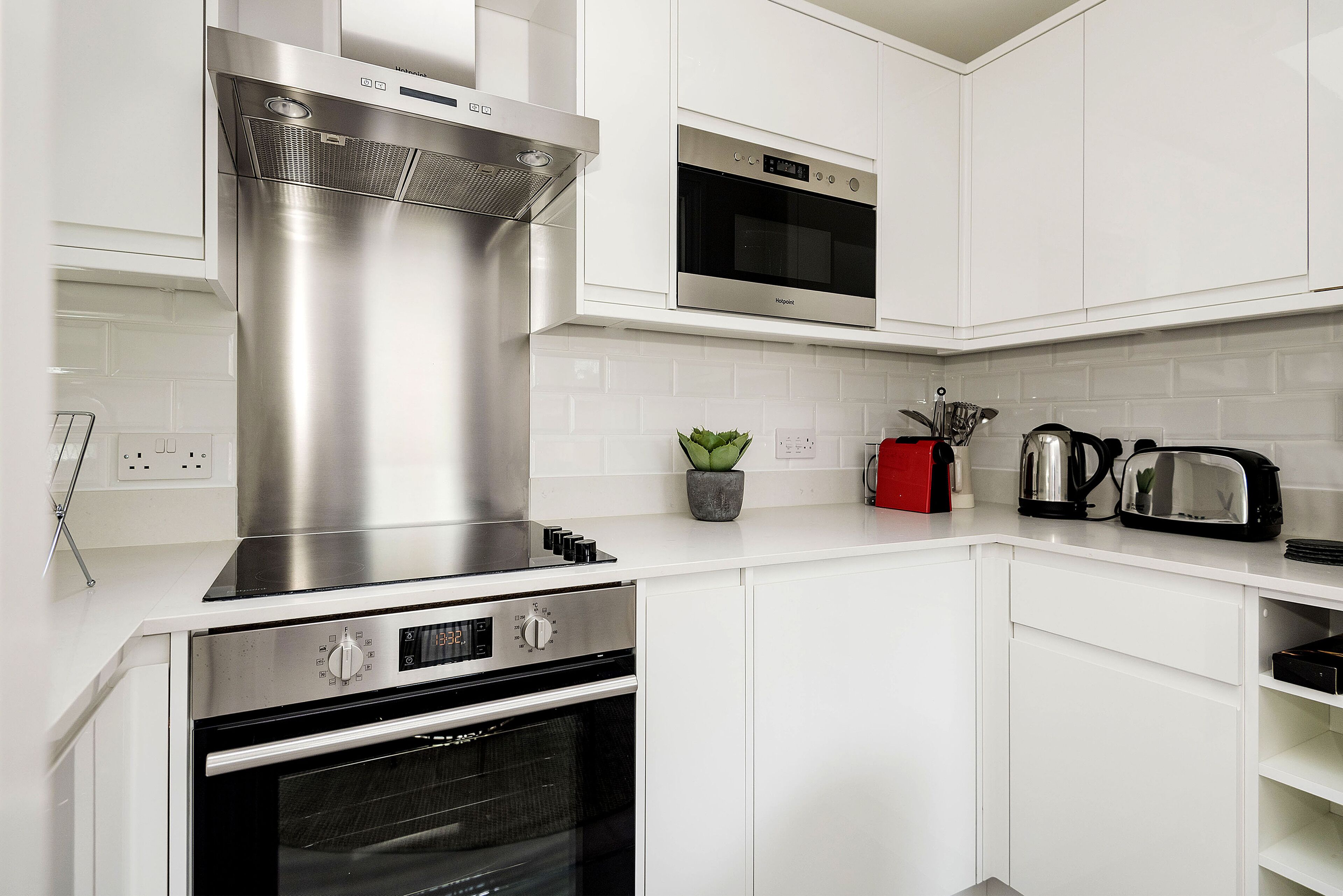 A modern kitchen with stainless steel appliances, white cabinetry, and a small potted plant.