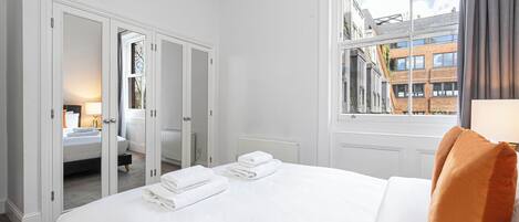 A hotel room with a large bed, a view of the city through a window, and a wardrobe with a mirror.
