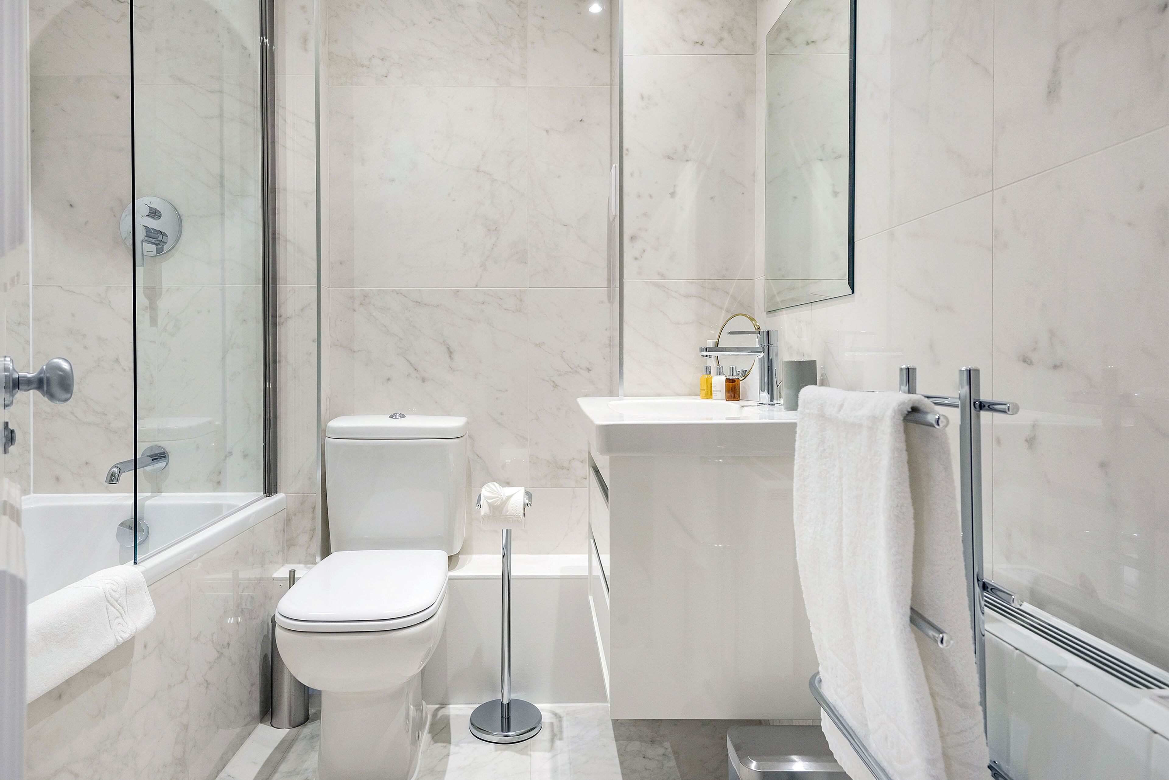 Een moderne badkamer met een douchecabine van glas, een toilet, een wastafel met een handdoekhouder en een spiegel.