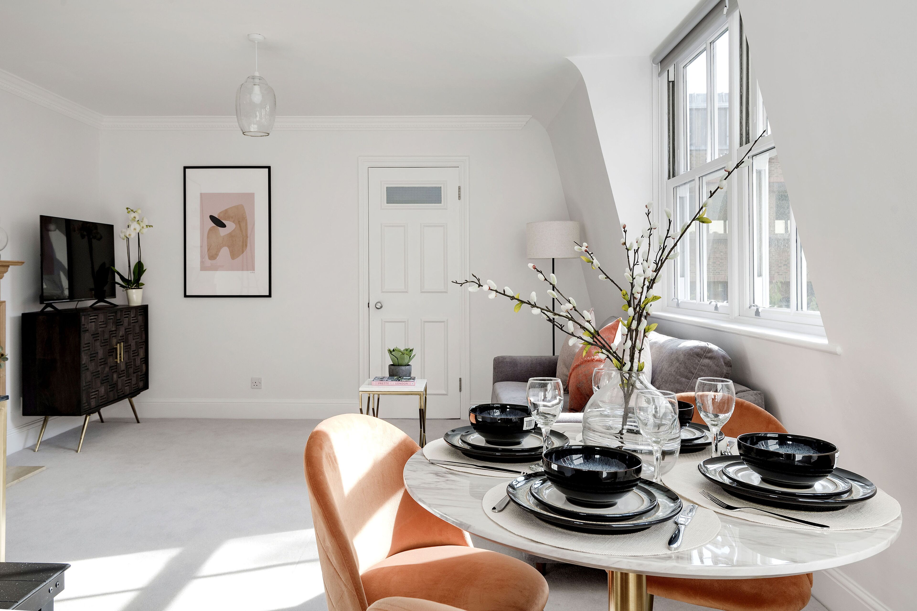 A dining area with a round table set for four, a black cabinet, and a framed artwork on the wall.