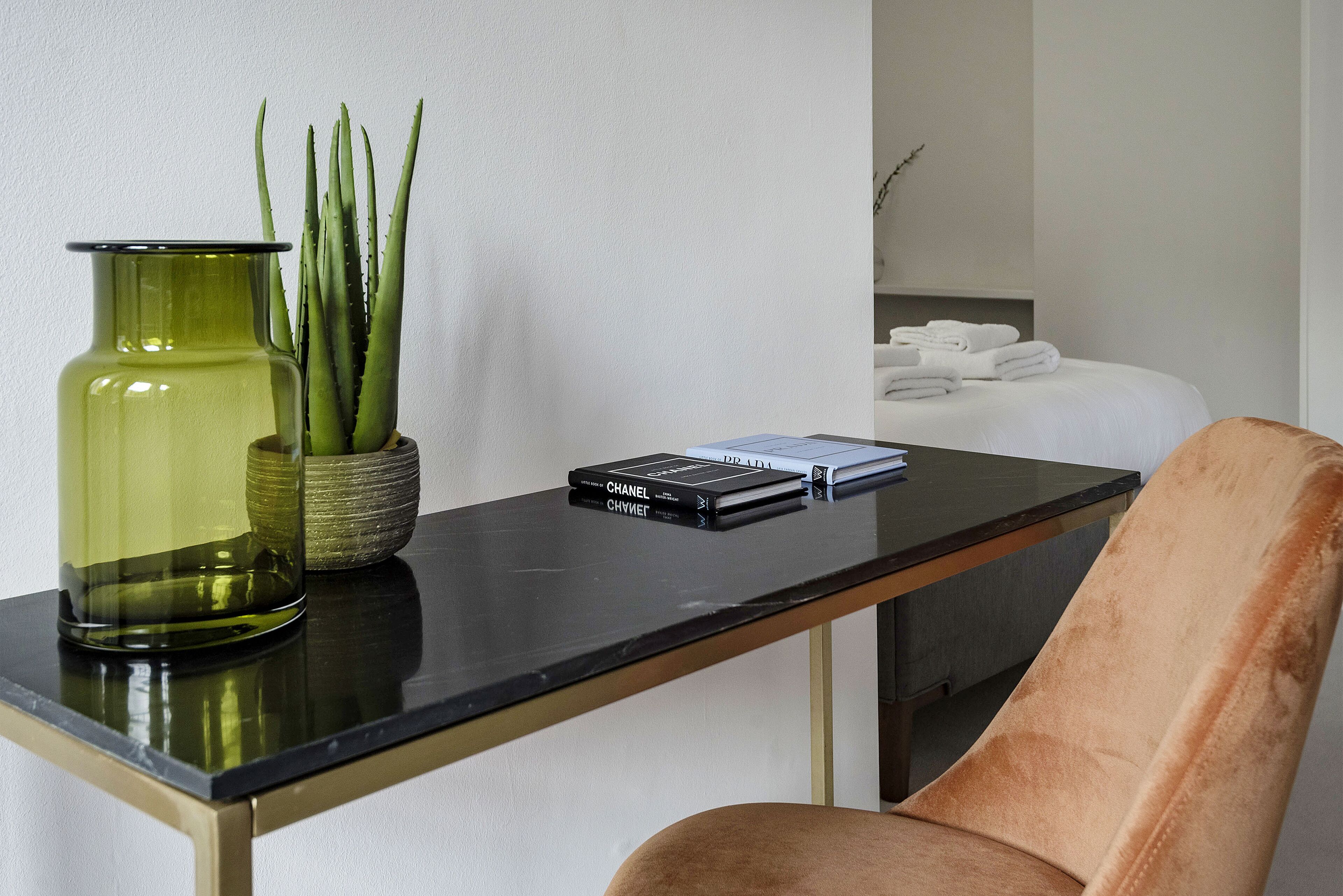 A modern room with a black glass table, a green vase with plants, and a plush brown chair.