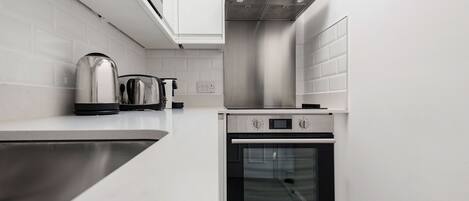 A compact kitchen with a stainless steel range hood, a built-in oven, and a kettle on the countertop.