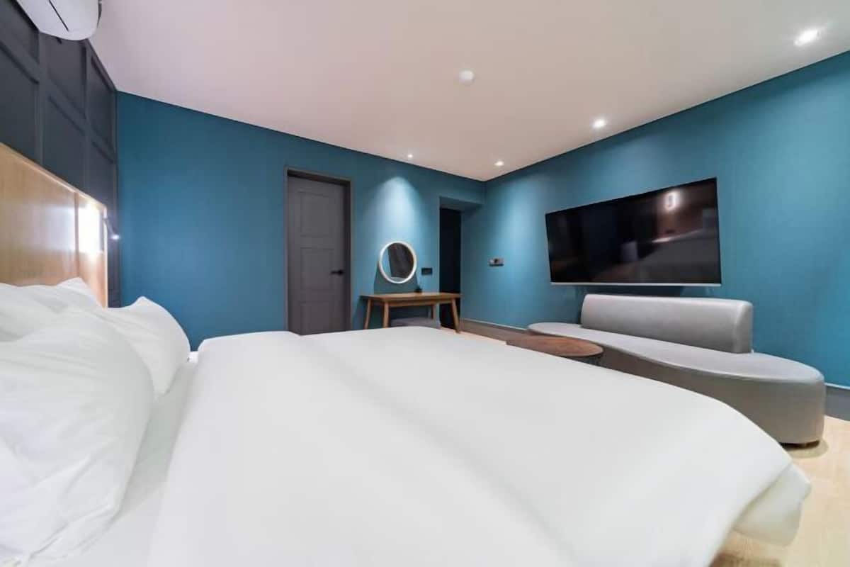 A modern bedroom with a large bed, a round mirror, a TV, and a seating area.