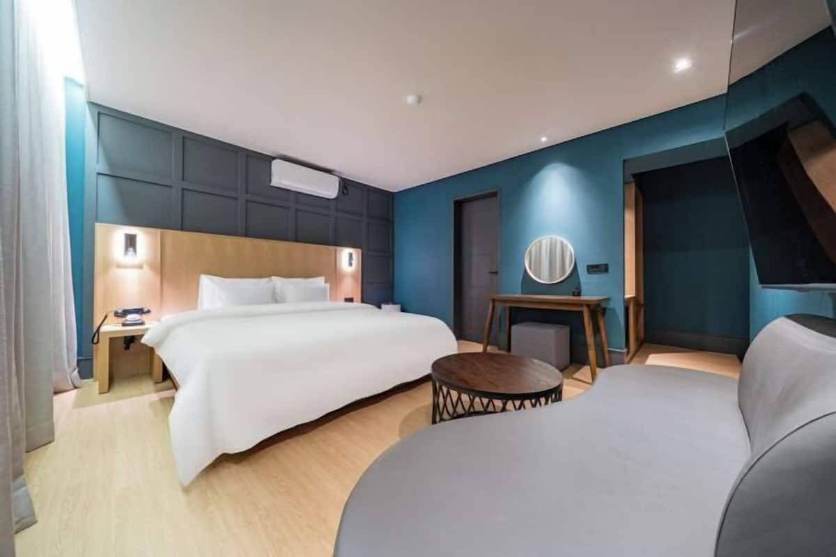 A modern hotel room with a large bed, bedside tables, a round table, and a sofa.