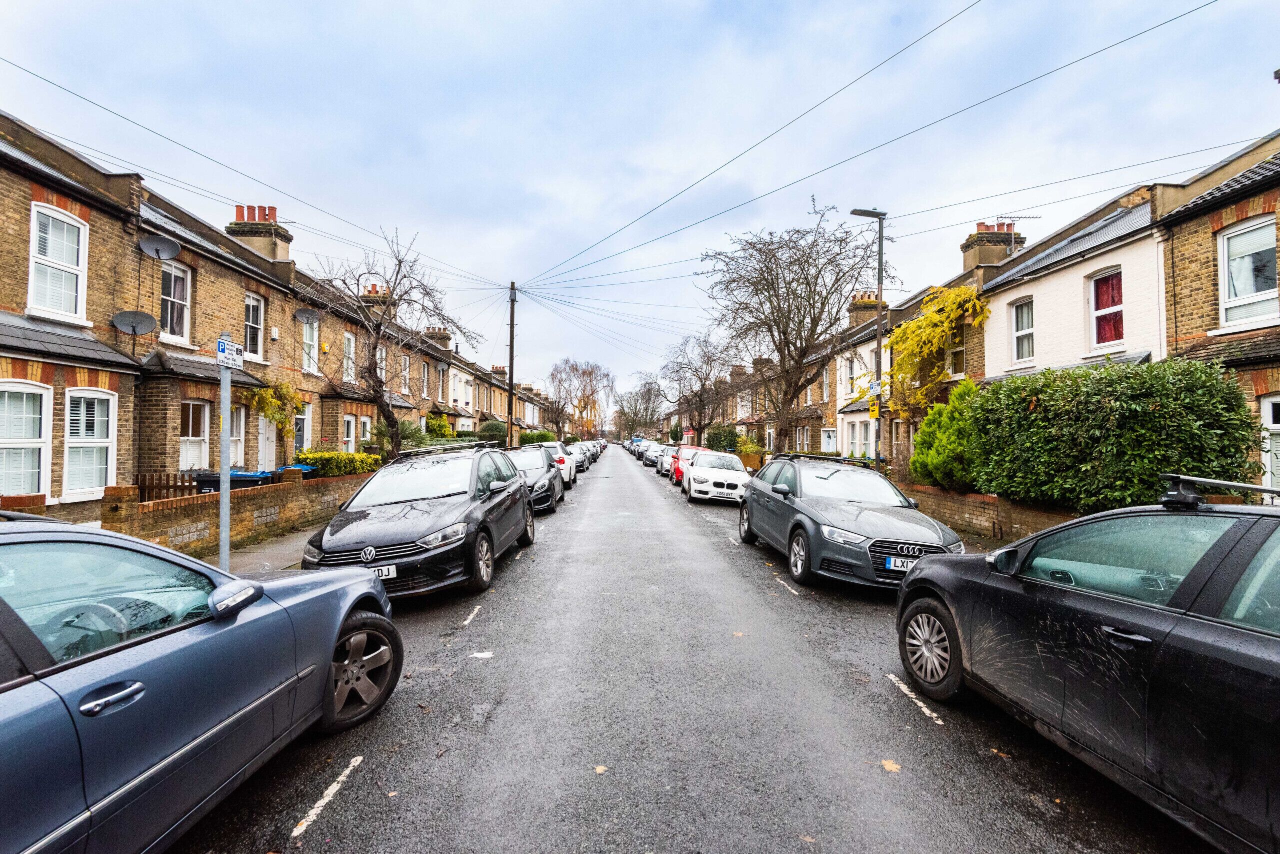 A residential street with parked cars and terraced houses on both sides.