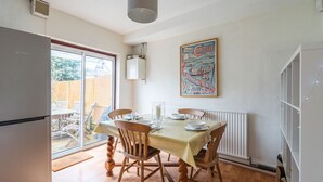 Un coin repas avec une table dressée pour quatre personnes, des chaises en bois, un radiateur et une fenêtre donnant sur un jardin.