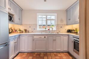 Une cuisine avec des meubles blancs, un pare-feu en carreaux, une fenêtre et une horloge au mur.