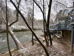 A riverside hotel with a deck overlooking the water, stone walls, and bare trees.