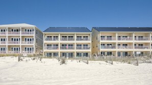 Un hôtel situé en bord de mer, doté de nombreux balcons, avec une plage de sable fin juste en face et un ciel bleu azur.