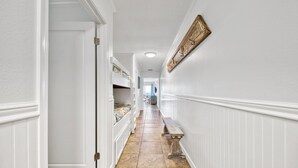 Un couloir étroit aux murs blancs, avec un banc en bois et une porte sur le côté gauche.