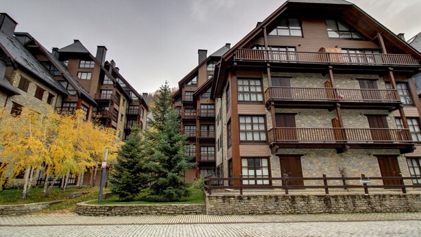 Ein mehrstöckiges Hotel mit einer Steinfassade, hölzernen Balkonen und einem zentralen Innenhof mit Bäumen.