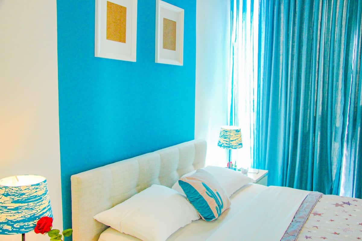 A bedroom with a blue wall, a white bed, and a window with blue curtains.