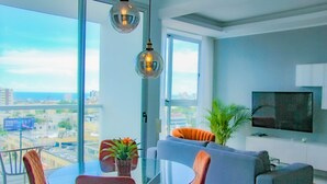 Una sala de estar moderna con una mesa de vidrio, sillas naranjas, un sofá gris y un televisor en la pared.