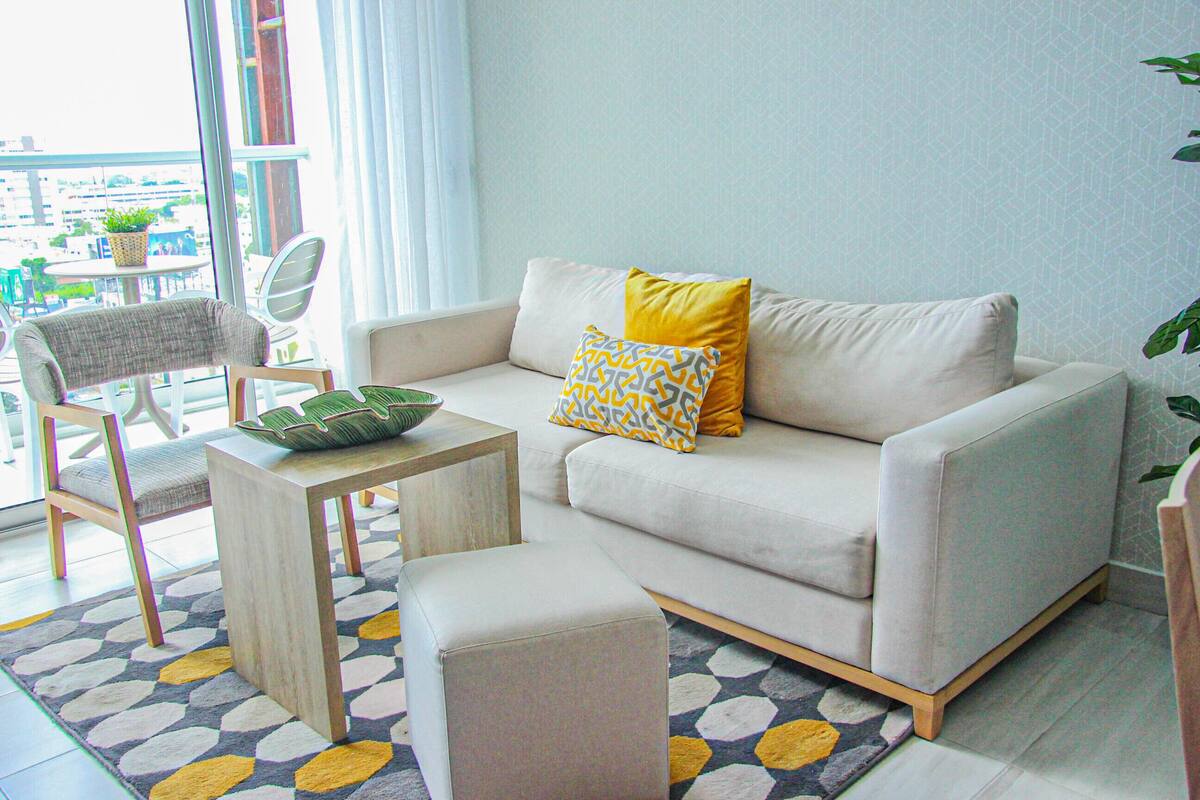 A modern living room with a sofa, ottoman, and a small table.