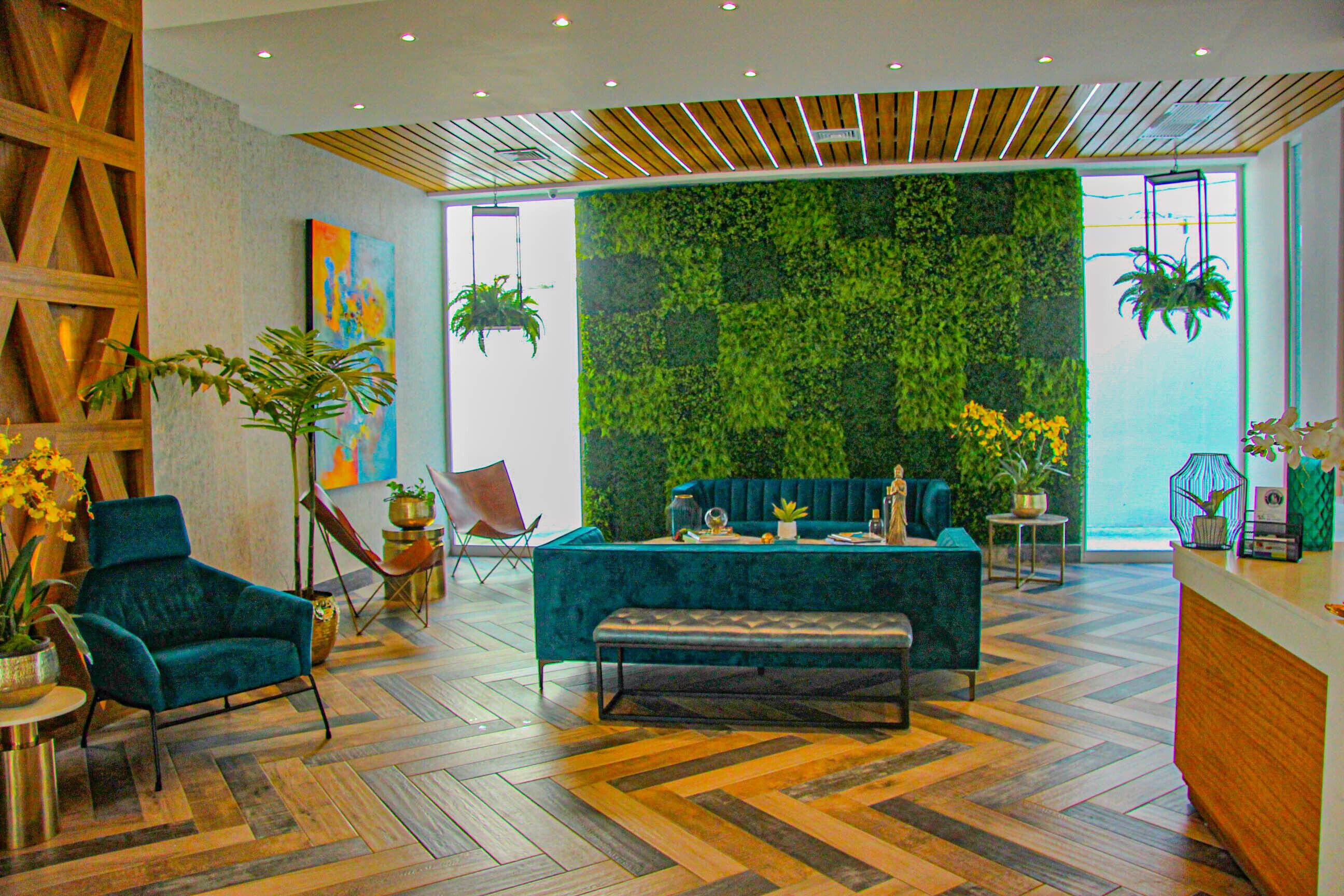 Un hall d’entrée moderne avec un parquet en bois disposé en chevrons, un canapé recouvert d’un tissu vert, un fauteuil turquoise et un comptoir d’accueil en bois.