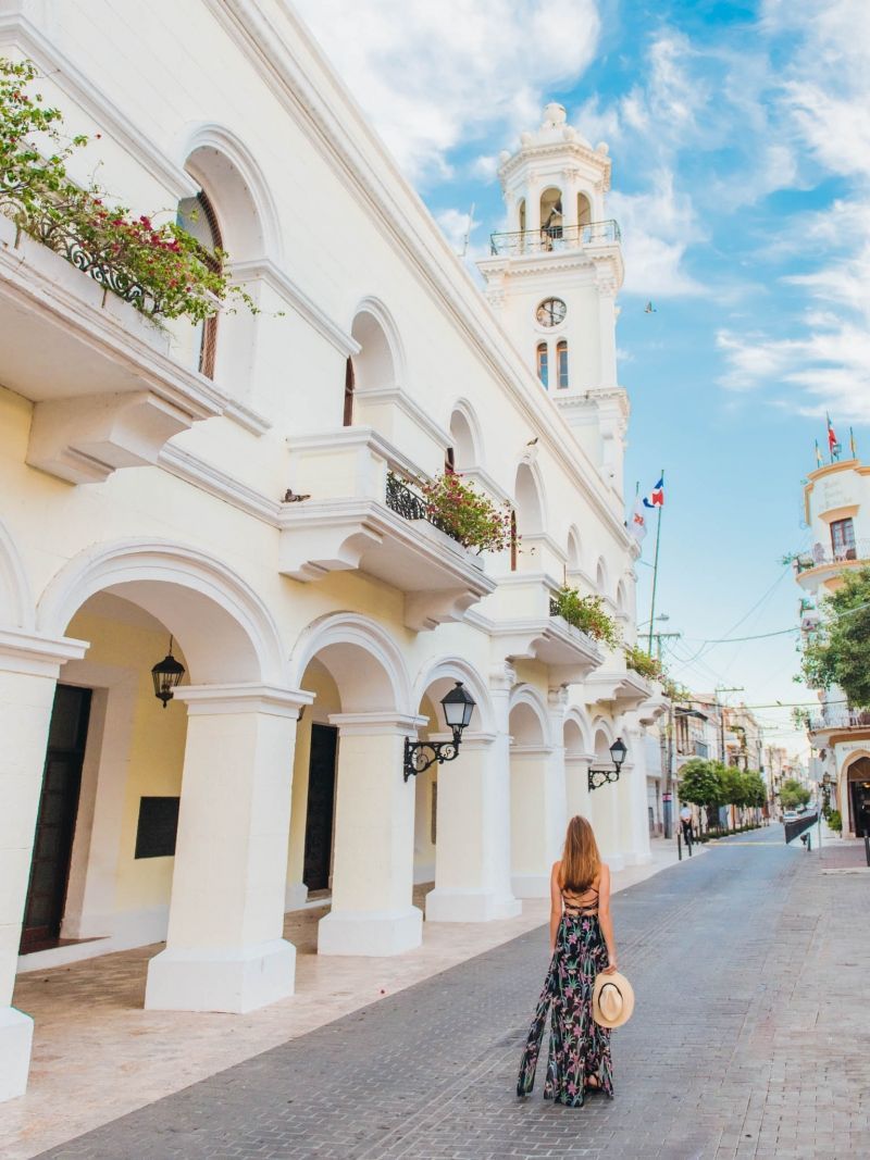 Um edifício com torre de relógio, janelas em arco e varandas com plantas.