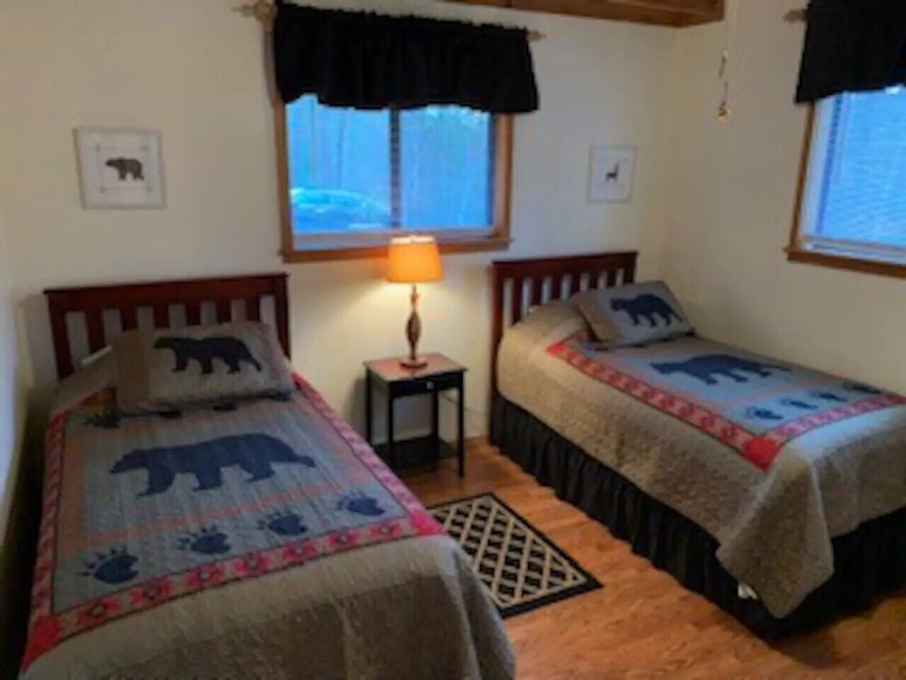 Ein Schlafzimmer mit zwei Betten, jeweils mit Bezug im Eisbären-Design, einem kleinen Tisch mit Lampe und einem Fenster mit Vorhängen.