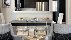 Un comedor moderno con una mesa de vidrio, sillas transparentes y un candelabro central.