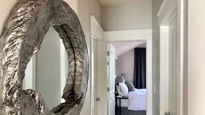 Habitación de hotel con un espejo circular grande de metal en la pared, una cama con ropa blanca, una mesita de noche con lámpara y una cortina oscura en la ventana.