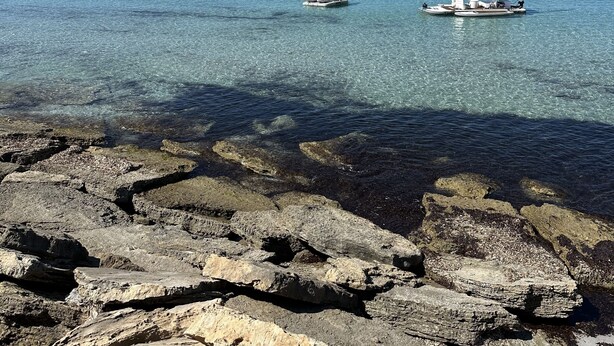 A rocky shoreline with clear blue water and two boats.