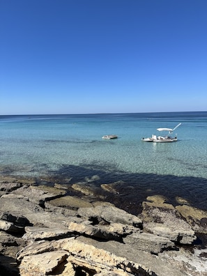 A rocky shoreline with clear blue water and two boats.