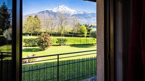 A balcony with a view of a snow-capped mountain, a well-maintained garden, and a clear sky.