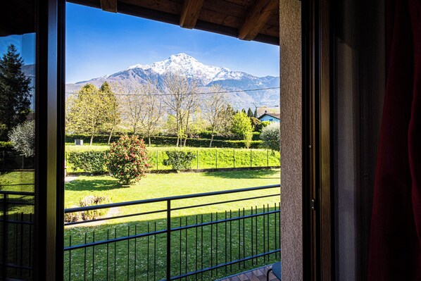 A balcony with a view of a snow-capped mountain, a well-maintained garden, and a clear sky.