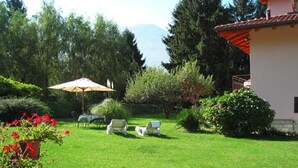 A well-maintained lawn with outdoor seating, a patio umbrella, and a building with a red roof.