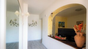 An interior with a wooden floor, white walls, a mirror, and a vase with flowers.