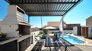 Eine Außenpatio mit Grill, Pool, Liegestühlen und einem Esstisch.