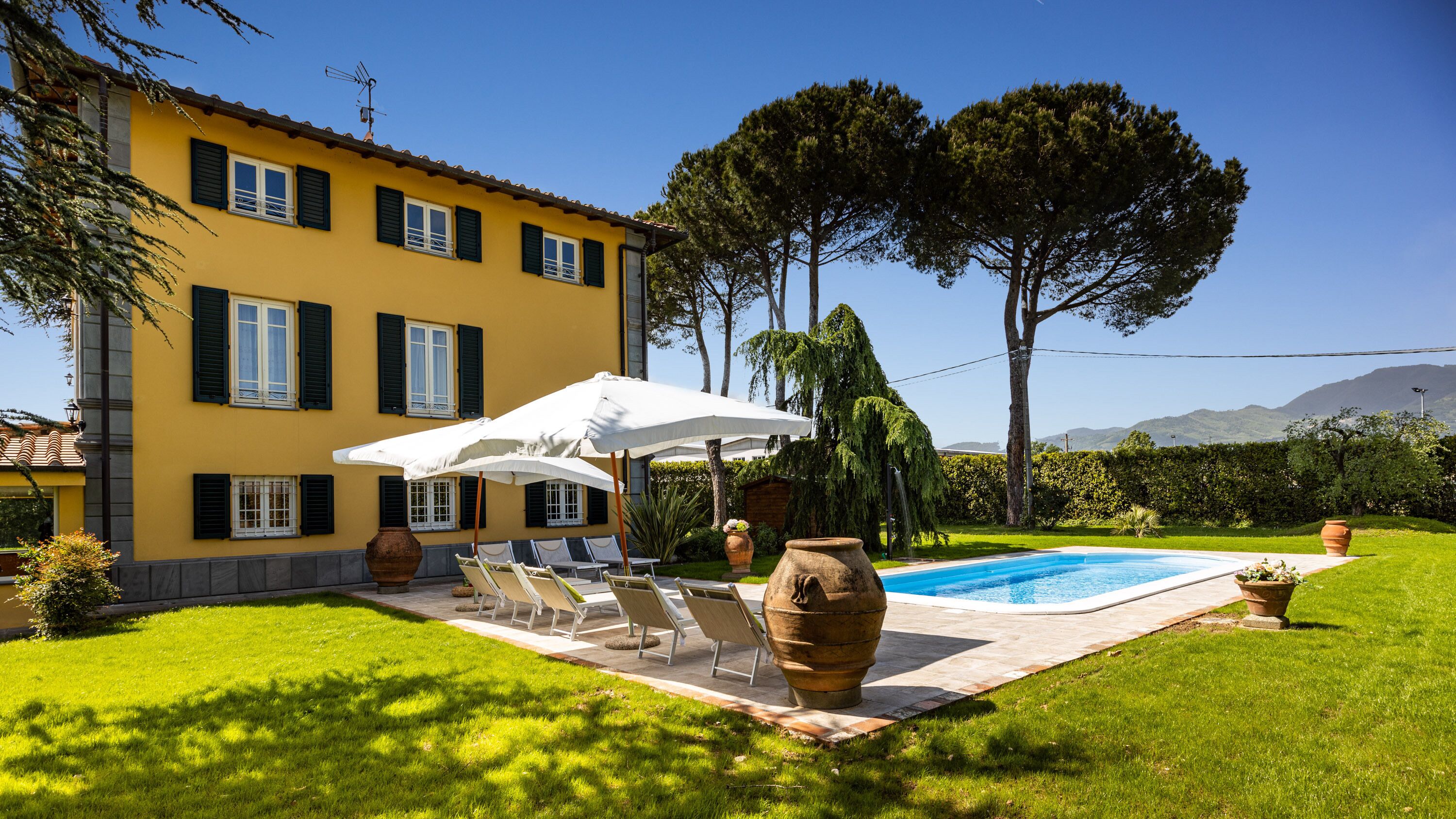 Eine gelbe Villa mit Swimmingpool, Sitzgelegenheiten im Freien und Bergblick.