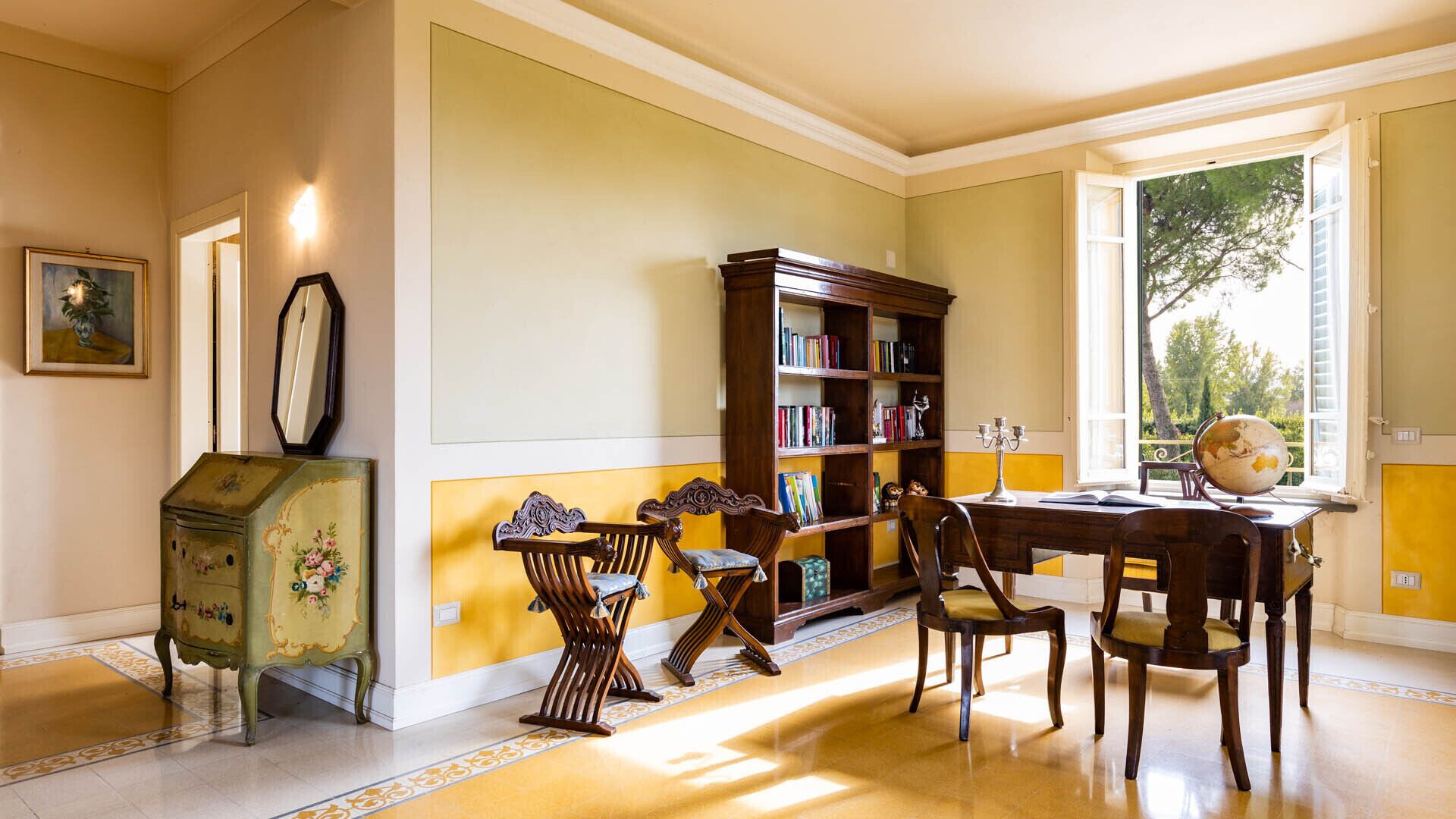 Een kamer met een houten bureau, stoelen, een boekenkast en een wereldbol.