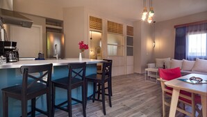 Una cocina moderna con una isla central, taburetes de bar y una cafetera. Hay un comedor con una mesa y sillas, y una sala de estar con un sofá y una mesa baja.