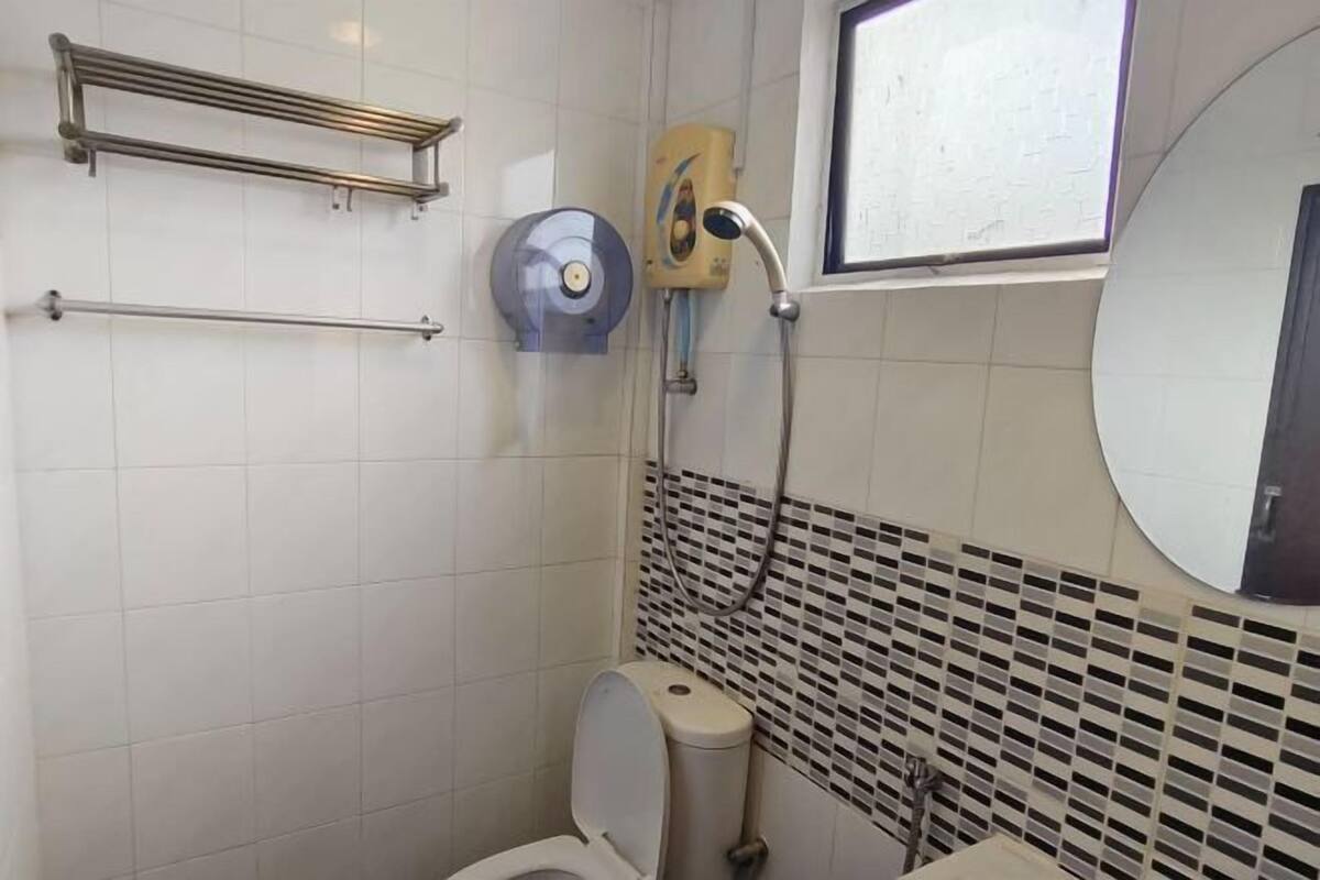 A bathroom with a toilet, a towel rack, a hand dryer, and a showerhead.