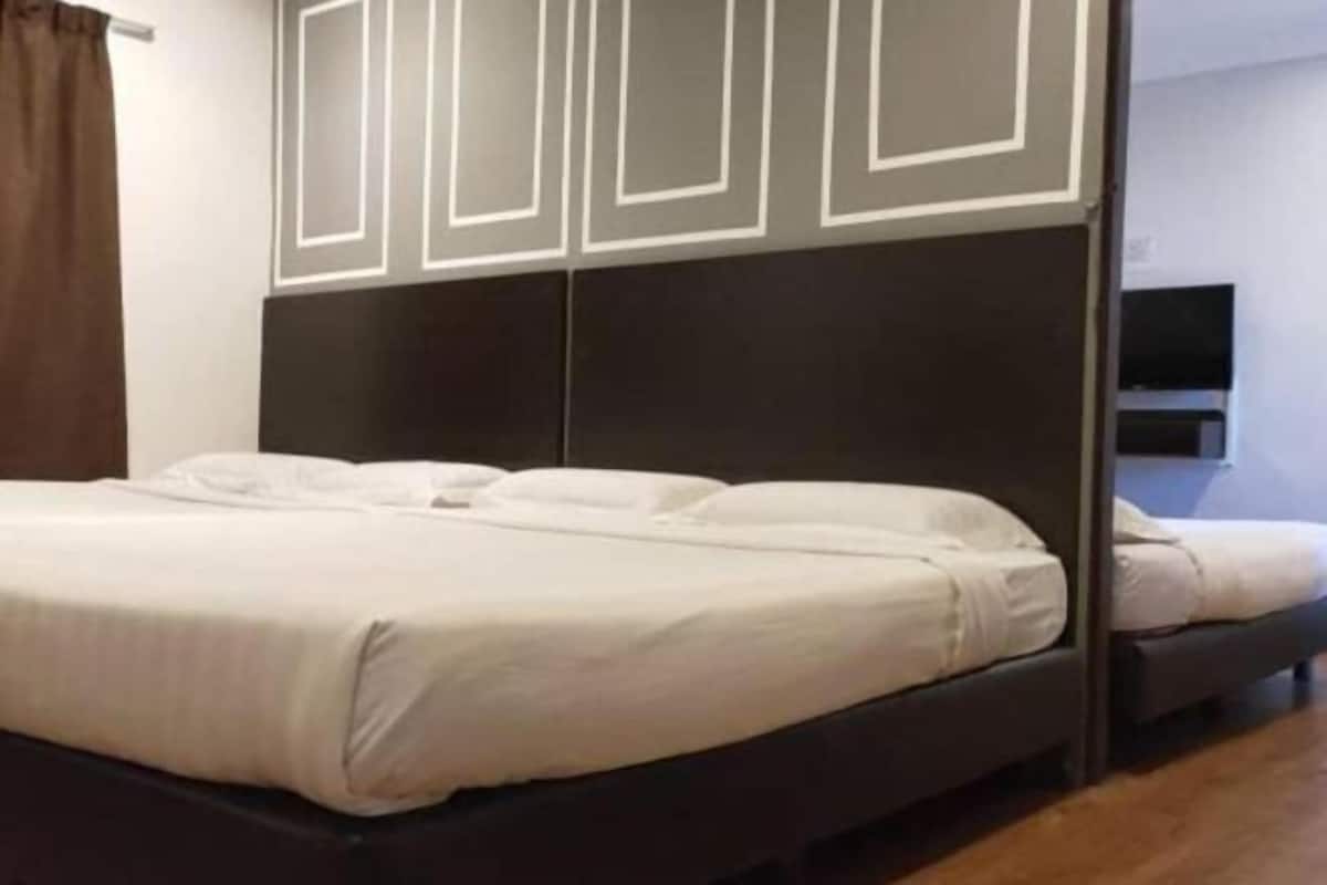 A single bed with a dark headboard, a flat-screen TV mounted on the wall, and a wooden floor.