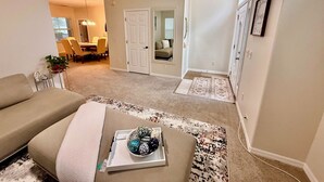 A living room with a beige sofa, a coffee table with decorative items, and a dining area in the background. - Grand Village 4BR Pool Home near Disney World (Davenport)