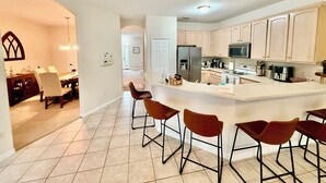 A modern kitchen with a central island, bar stools, and a dining area with a chandelier. - Grand Village 4BR Pool Home near Disney World (Davenport)