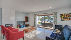 A modern living room with a flat-screen TV, red chairs, a blue sofa, and a view of a pool and outdoor furniture. - ★Stunning Luxury Villa w/Private Pool, n/Galé Beach, Albufeira (Albufeira)