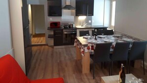 Een compacte keuken met moderne apparaten, een eethoek met een tafel voor vier personen, en een rode stoel op de voorgrond.