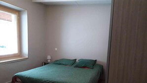 Een kleine eenpersoonskamer met een houten vloer, een raam en een nachtkastje met een lamp.