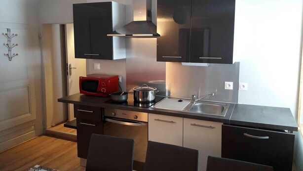 Een compacte keuken met donkere kastjes, een rode magnetron, een spoelbak en een fornuis.