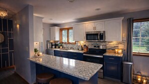 A modern kitchen with a central island, dark blue cabinets, stainless steel appliances, and a view of the outdoors. - Luxury Vacation home in the Poconos close to the lake and community pool.  (Albrightsville)