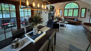 A spacious living room with a fireplace, a dining area with a glass-top table, and large windows offering a view of the outdoors. - Luxury Vacation home in the Poconos close to the lake and community pool.  (Albrightsville)