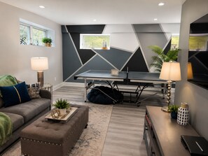 A modern living room with a ping pong table, a sofa, a coffee table, and a TV.