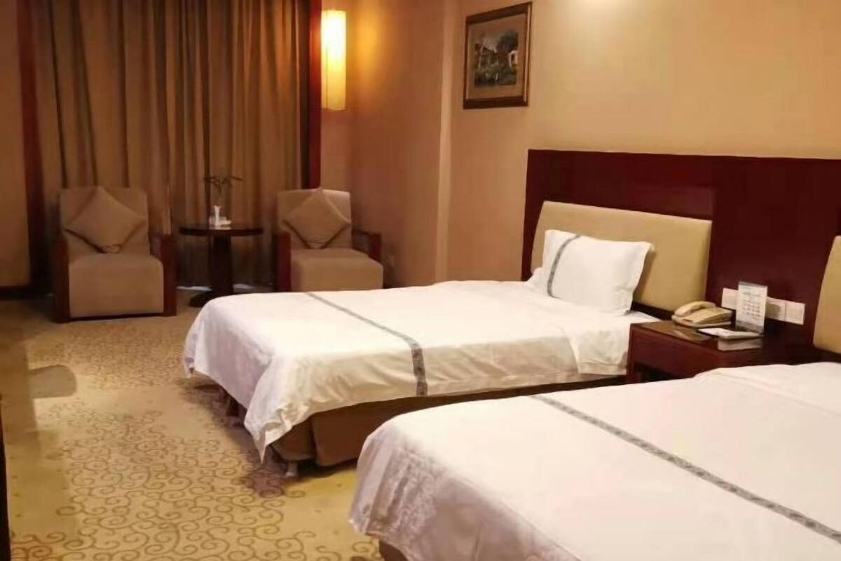 A hotel room with two beds, a small table, two chairs, a nightstand with a phone, and a painting on the wall.