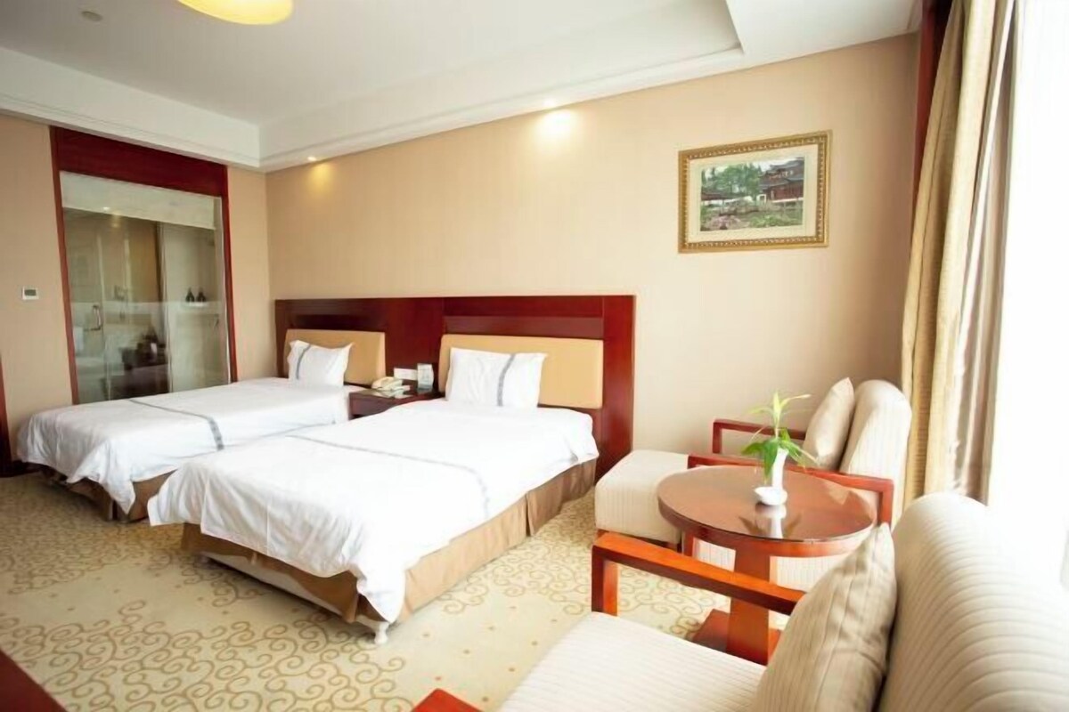 A hotel room with two beds, a small table, a sofa, a mirror, and a framed picture on the wall.