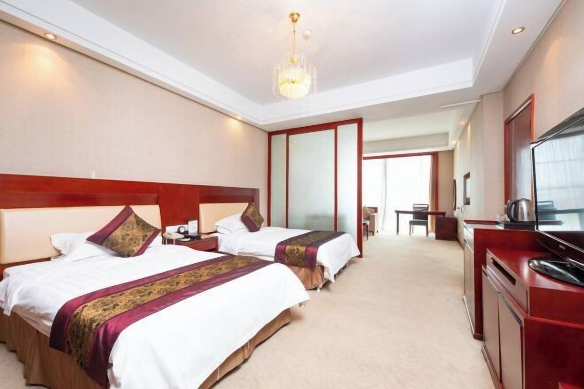 A hotel room with two beds, a TV, a desk, and a chair.
