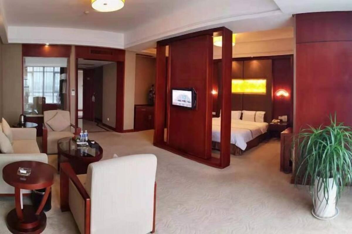 A hotel room with a bed, a TV, a seating area with a table and chairs, and a large mirror.